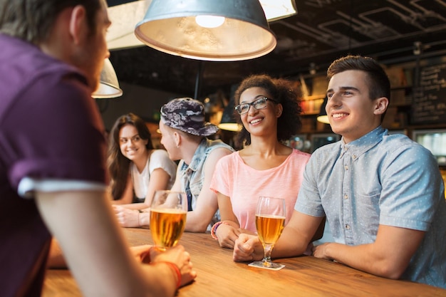 人、レジャー、友情、コミュニケーションのコンセプト – ビールを飲み、バーやパブで話す幸せな笑顔の友人のグループ