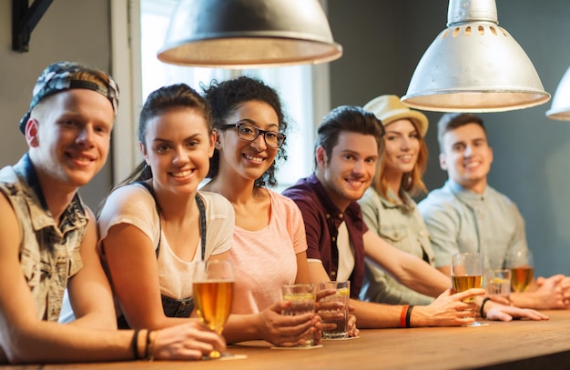 people, leisure, friendship and communication concept - group of happy smiling friends drinking beer, water or cocktails at bar or pub