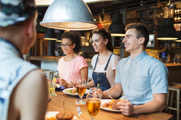 people, leisure, friendship and communication concept - group of happy smiling friends eating, drinking and talking at bar or pub