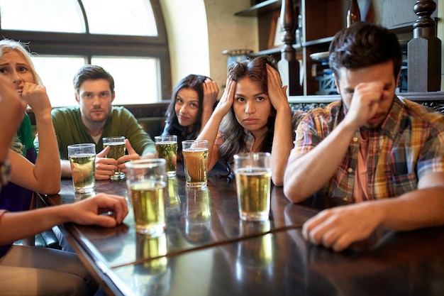 people, leisure, friendship and entertainment concept - friends drinking beer and watching sport game or football match at bar or pub