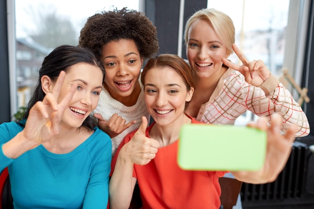 people, leisure, friendship, gesture and technology concept - happy young women taking selfie with smartphone and showing victory gesture