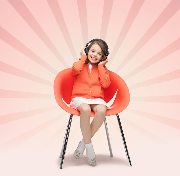 Концепция людей, досуга, хобби и развлечений - счастливая маленькая девочка слушает музыку в наушниках на фоне розовых лучей