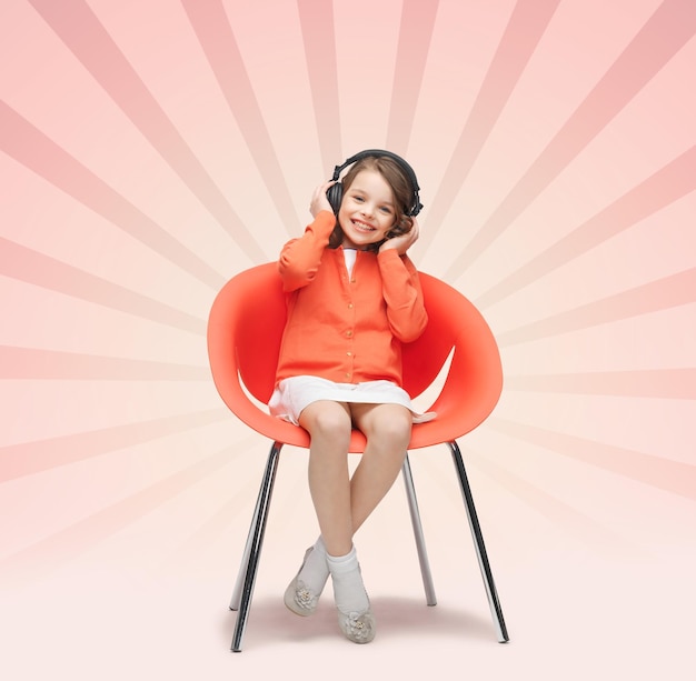 people, leisure, hobby and entertainment concept - happy little girl listening to music in headphones over pink burst rays background