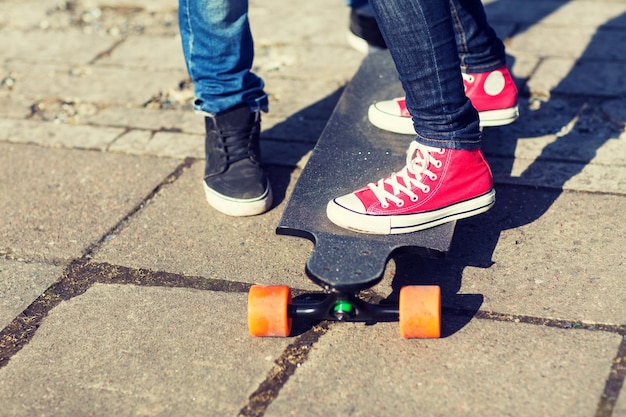 People, leisure and sport concept - close up of teenage couple\
feet with longboard on street