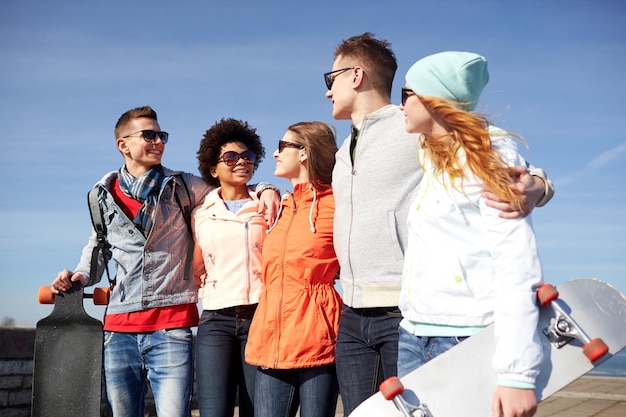 Photo people, leisure and sport concept - group of happy teenage friends with longboards talking on city street