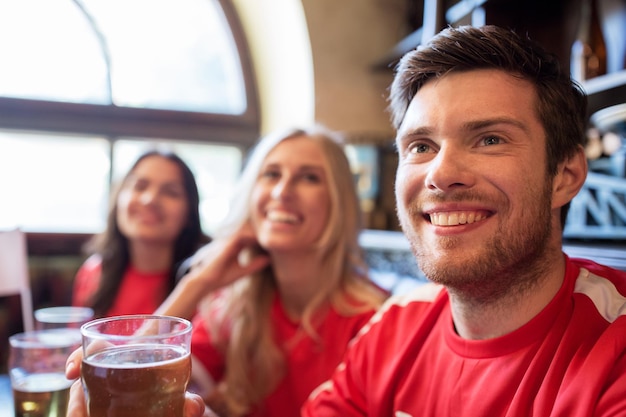 people, leisure and sport concept - happy friends or football fans drinking beer and watching soccer game or match at bar or pub