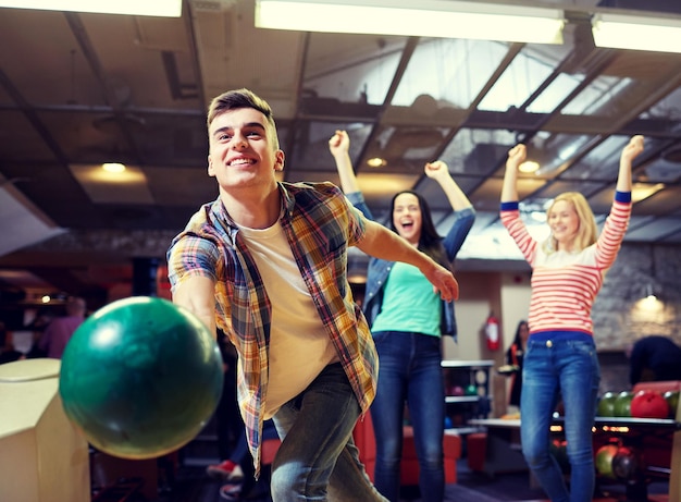 концепция людей, отдыха, спорта и развлечений - счастливый молодой человек, бросающий мяч в боулинг-клуб