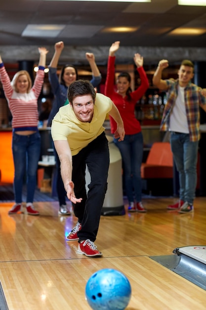 people, leisure, sport and entertainment concept - happy young man throwing ball in bowling club