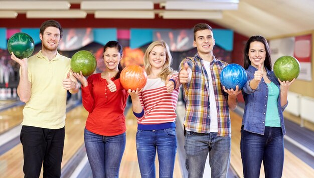 people, leisure, sport, friendship and entertainment concept - happy friends holding balls and showing thumbs up in bowling club