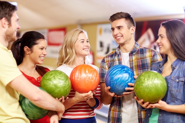 Concetto di persone, tempo libero, sport, amicizia e intrattenimento - amici felici che tengono le palle e parlano nel club di bowling