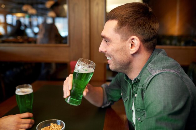 Photo people leisure and st patricks day concept happy young man drinking green beer at bar or pub