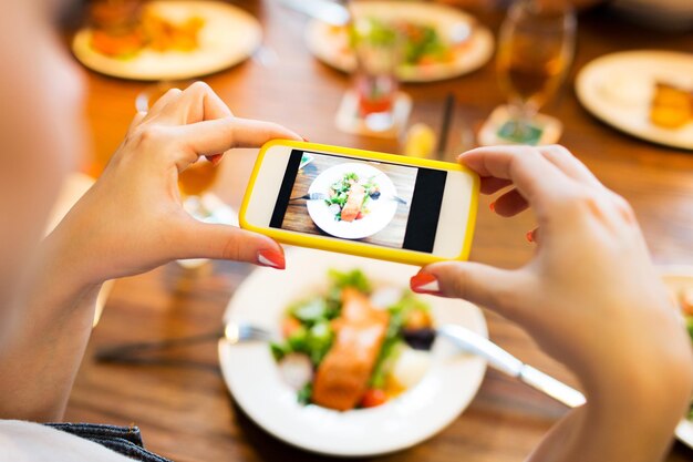 people, leisure, technology and internet addiction concept - close up of woman with smartphone photographing food at restaurant