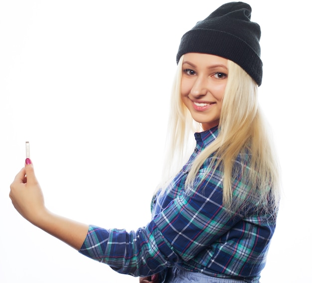 People, lifestyle and tehnology concept: pretty teen girl wearing hat, taking selfies with her smart phone - isolated on white