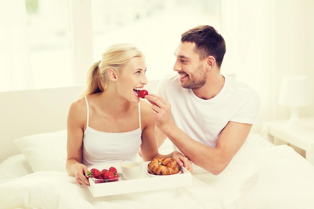 люди, любовь, забота и концепция счастья - счастливая пара завтракает в постели и ест клубнику дома