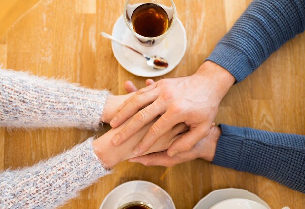 people, love, romance and dating concept - close up of happy couple drinking tea and holding hands at cafe or restaurant