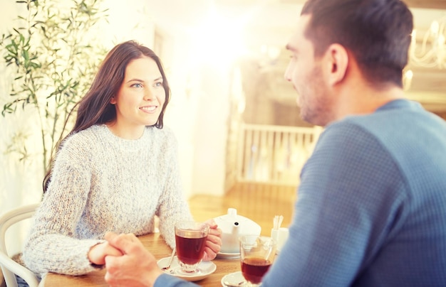 people, love, romance and dating concept - happy couple drinking tea and holding hands at cafe or restaurant