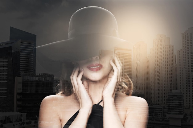 人、豪華さとファッションのコンセプト - 二重露出の背景を持つドバイ市の黒い帽子の美しい女性