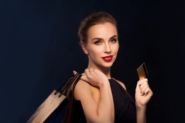 people, luxury and sale concept - beautiful woman with credit card and shopping bags over black background