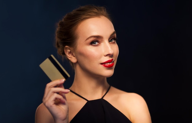 people, luxury, wealth, finances and shopping concept - beautiful woman with credit card over black background