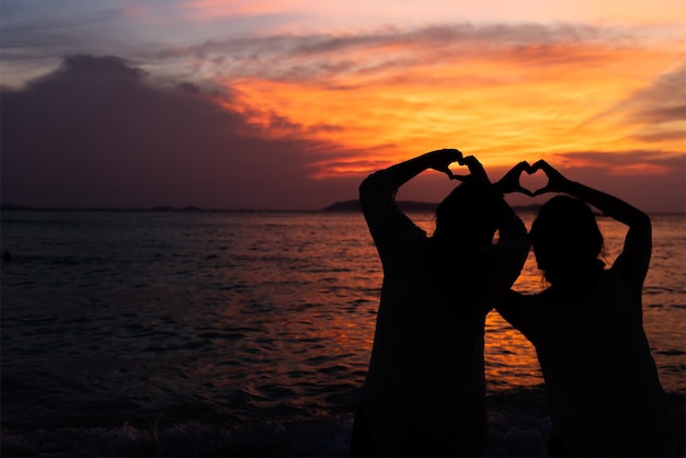 People makes heart symbol with hand at dusk