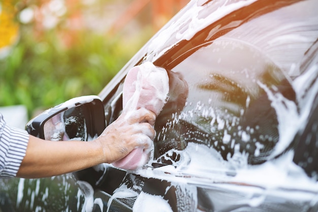 People man holding hand pink sponge for washing car. cleaning wheel tire. Concept car wash clean.