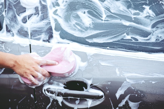 People man holding hand pink sponge for washing car. cleaning wheel tire. Concept car wash clean.