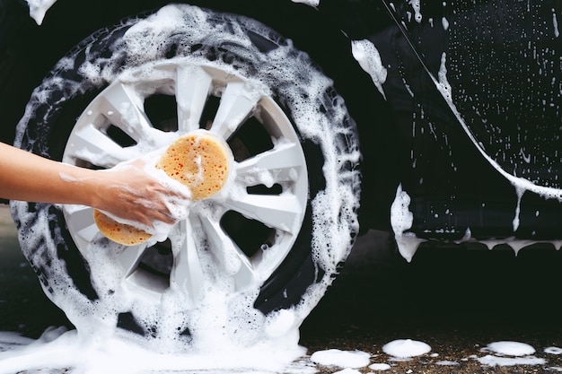 People man holding hand yellow sponge for washing car. cleaning\
wheel tire. concept car wash clean.