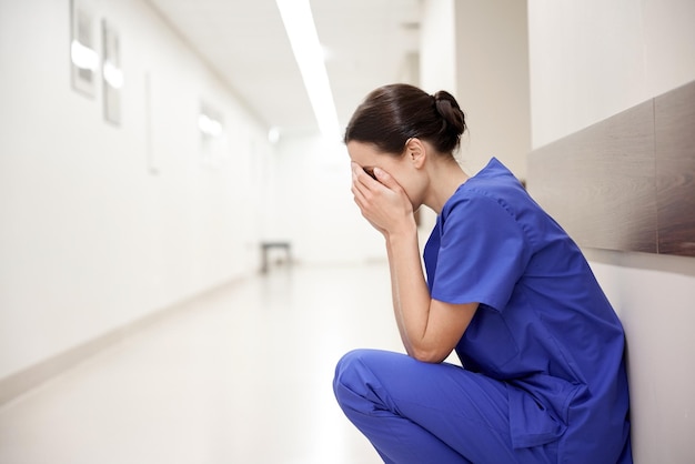 people, medicine, healthcare and sorrow concept - sad or crying female nurse at hospital corridor