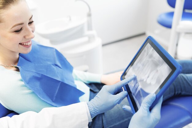 Foto persone, medicina, stomatologia e concetto di assistenza sanitaria - primo piano delle mani del dentista che mostrano i raggi x teeht sul computer tablet pc alla donna paziente presso l'ufficio della clinica odontoiatrica