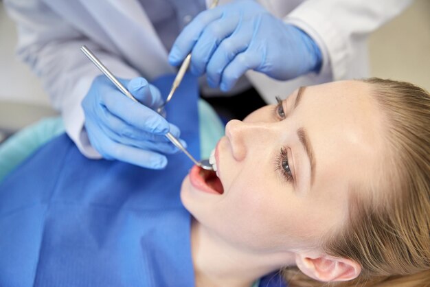 人、医学、口腔病学、ヘルスケアのコンセプト – デンタルミラーを使った歯科医の手のクローズアップと、歯科医院で女性患者の歯をチェックするプローブ