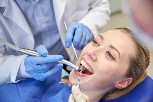 사람, 의학, 구강 및 건강 관리 개념 - 치과 진료소에서 여성 환자의 치아를 치료하는 거울, 드릴 및 치과용 공기 물총 스프레이를 사용하여 치과의사와 조수를 마감합니다.