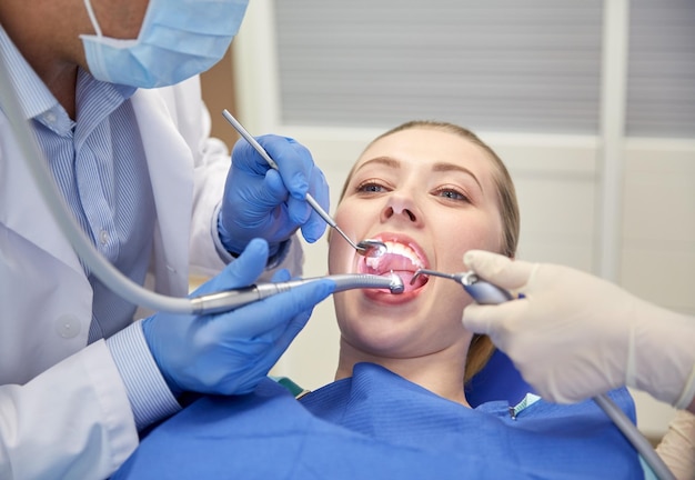 사람, 의학, 구강 및 건강 관리 개념 - 치과 진료소에서 여성 환자의 치아를 치료하는 거울, 드릴 및 치과용 공기 물총 스프레이를 사용하여 치과의사와 조수를 마감합니다.