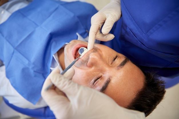 people, medicine, stomatology and health care concept - close up of female dentist with dental mirror checking up male patient teeth at dental clinic office