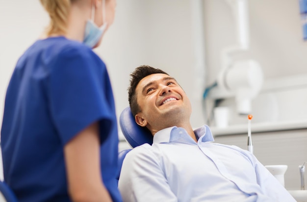 people, medicine, stomatology and health care concept - female dentist talking to happy male patient at dental clinic office