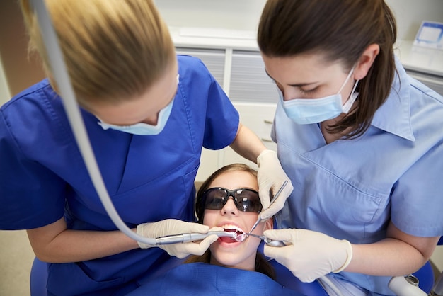 people, medicine, stomatology and health care concept - female dentists with mirror, drill and probe treating patient girl teeth at dental clinic office