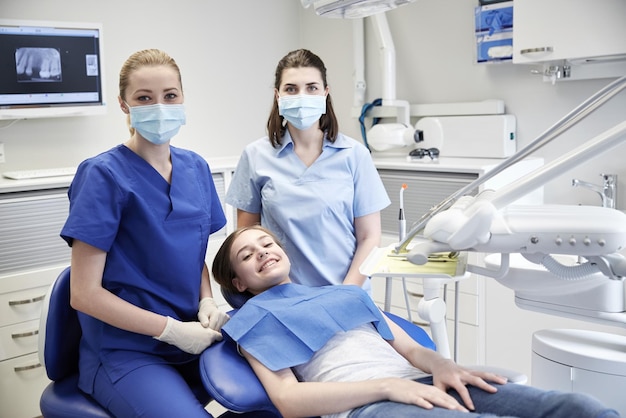 люди, медицина, стоматология и концепция здравоохранения - счастливая женщина-стоматолог с ассистентом и пациенткой в офисе стоматологической клиники