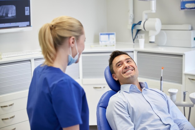 people, medicine, stomatology and health care concept - happy female dentist with man patient talking at dental clinic office