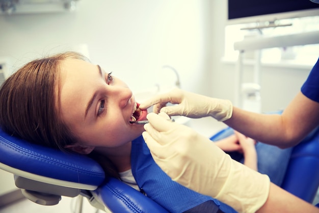 people, medicine, stomatology and health care concept - happy female dentist with mirror checking patient girl teeth up at dental clinic office