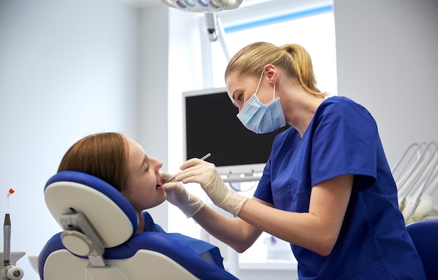 people, medicine, stomatology and health care concept - happy female dentist with mirror checking patient girl teeth up at dental clinic office