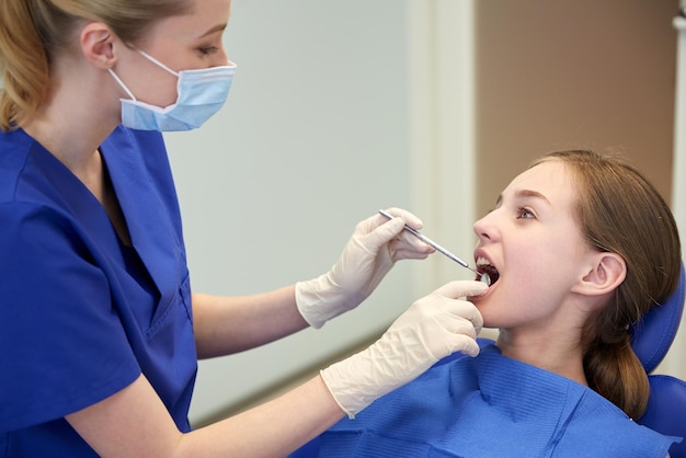 people, medicine, stomatology and health care concept - happy female dentist with mirror checking patient girl teeth up at dental clinic office