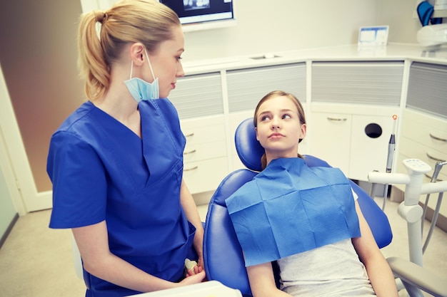 people, medicine, stomatology and health care concept - happy female dentist with patient girl talking at dental clinic office