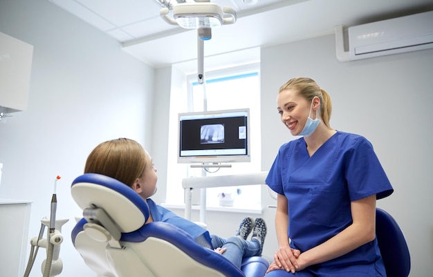 people, medicine, stomatology and health care concept - happy female dentist with patient girl talking at dental clinic office