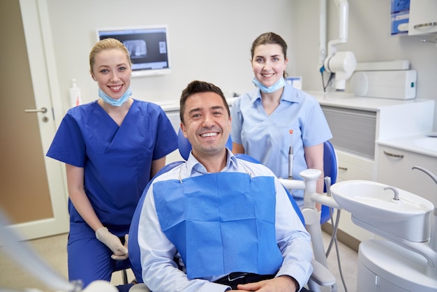 people, medicine, stomatology and health care concept - happy female dentists with man patient at dental clinic office