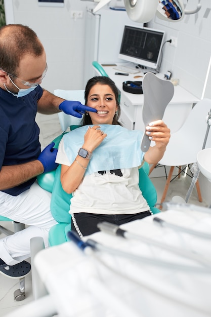 Foto persone, medicina, stomatologia e concetto di assistenza sanitaria - dentista maschio felice che mostra piano di lavoro al paziente donna presso l'ufficio della clinica odontoiatrica.