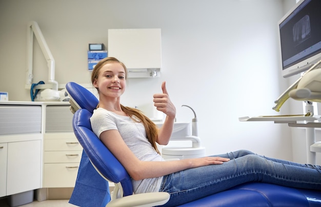 Concetto di persone, medicina, stomatologia e assistenza sanitaria - ragazza paziente felice che mostra i pollici in su presso l'ufficio della clinica dentale