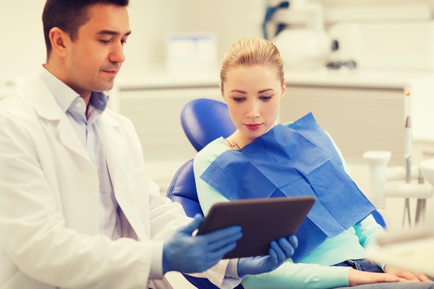 Photo people, medicine, stomatology and health care concept - male dentist showing tablet pc computer to woman patient at dental clinic office