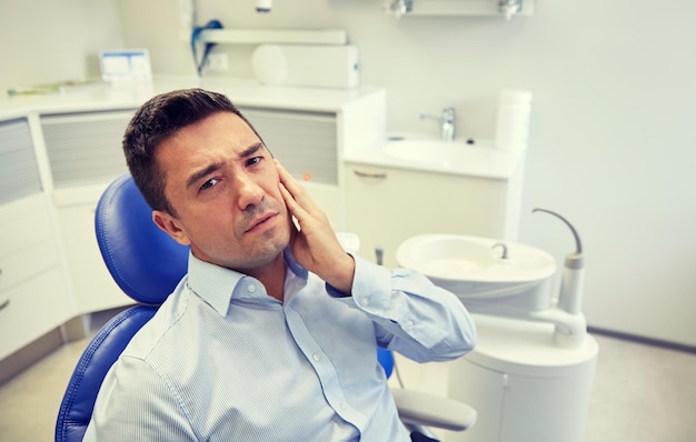 People, medicine, stomatology and health care concept - unhappy male patient having toothache sitting on dental chair at clinic office