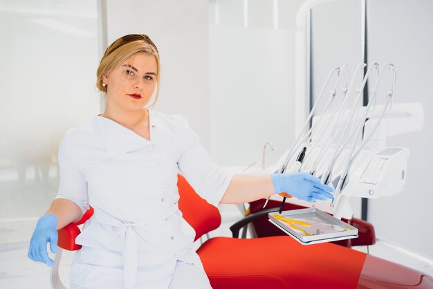 Photo people, medicine, stomatology and healthcare concept - happy young female dentist with tools over medical office background