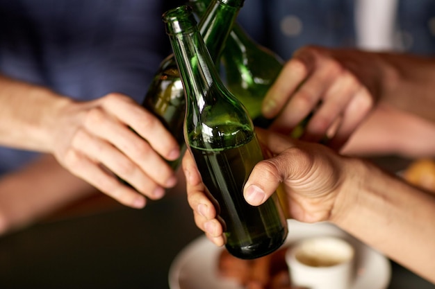 people, men, leisure, friendship and celebration concept - close up of male friends drinking beer and clinking bottles at bar or pub