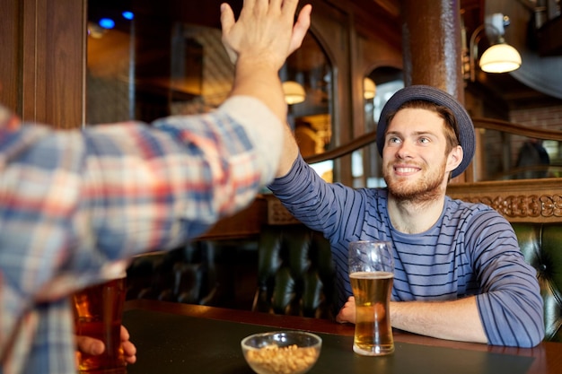 люди, мужчины, досуг, дружба и концепция жестов - счастливые друзья-мужчины, пьющие бочковое пиво и дающие пять в баре или пабе